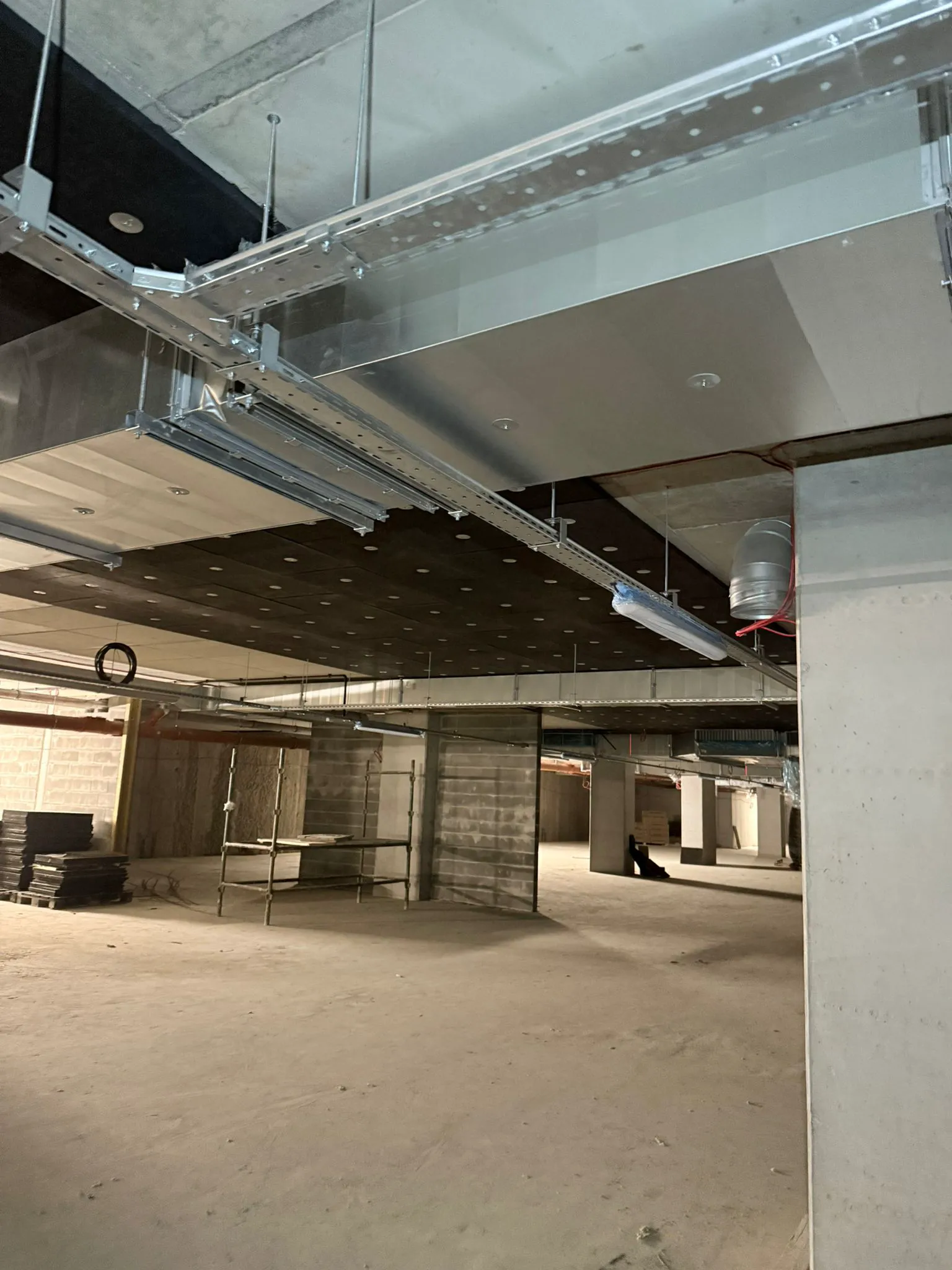 Wnętrze budynku w stanie surowym z widocznymi stelażami sufitowymi i kanałami wentylacyjnymi