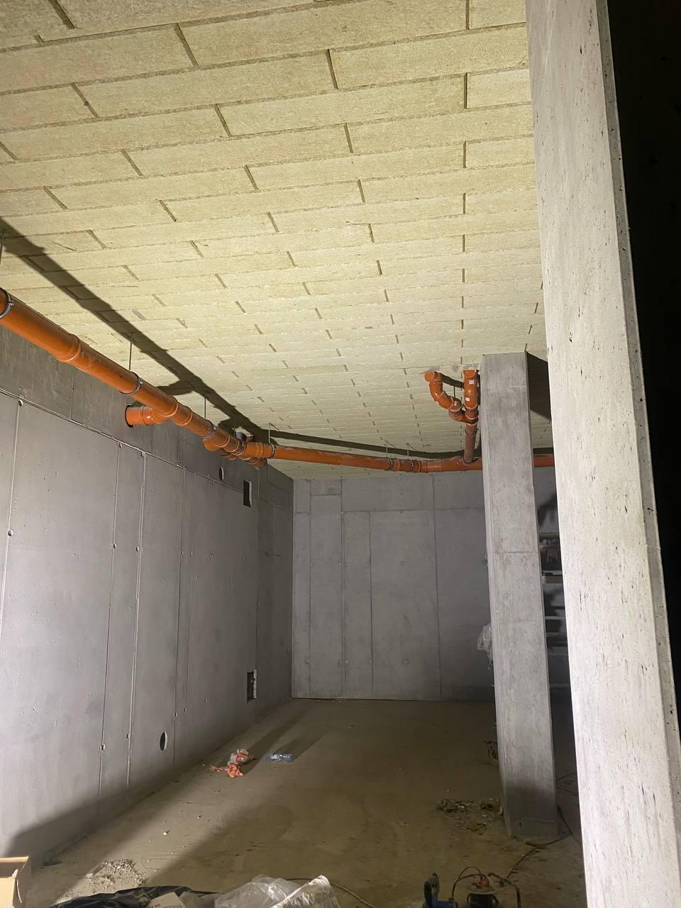 Ocieplenie stropu wełną mineralną w pomieszczeniu z betonowymi ścianami i pomarańczowymi rurami