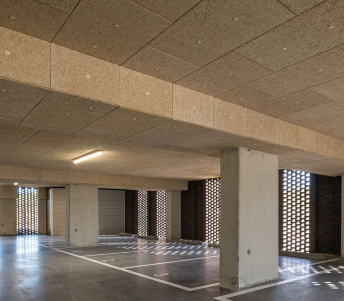 Wnętrze garażu podziemnego z betonowymi filarami, oświetlonym sufitem i wyznaczonymi miejscami parkingowymi